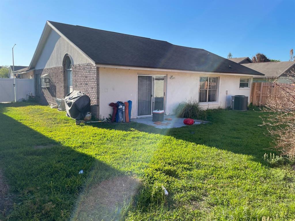 The backyard of a single-story house features a concrete patio, sliding glass door, and lawn — 2158 PAPRIKA DRIVE, ORLANDO, FL