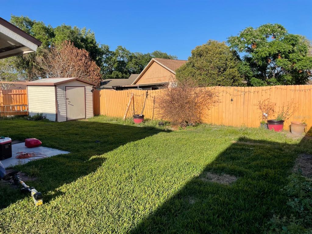 A grassy backyard features a storage shed, a wooden fence, and a concrete patio area — 2158 PAPRIKA DRIVE, ORLANDO, FL