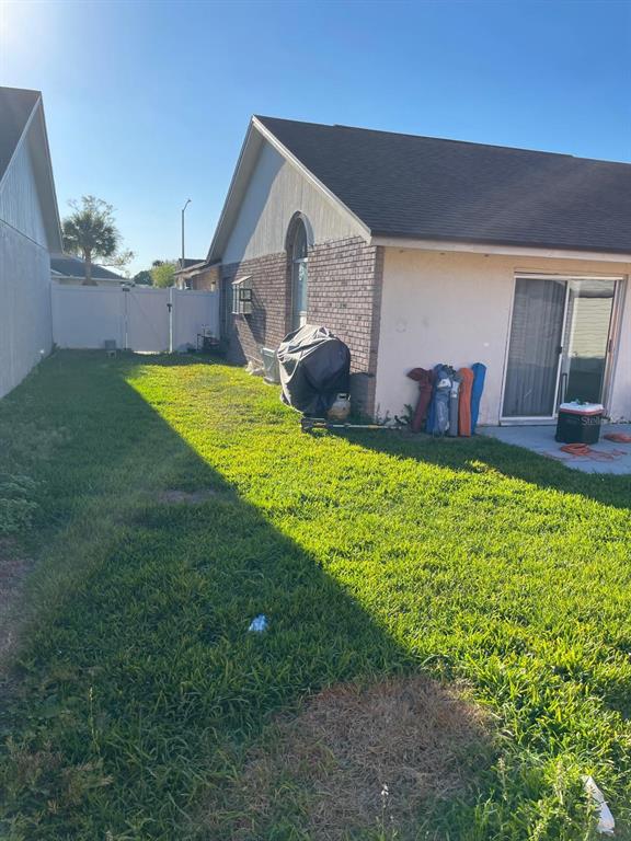 A side view of a house exterior with a grassy yard and a white fence — 2158 PAPRIKA DRIVE, ORLANDO, FL