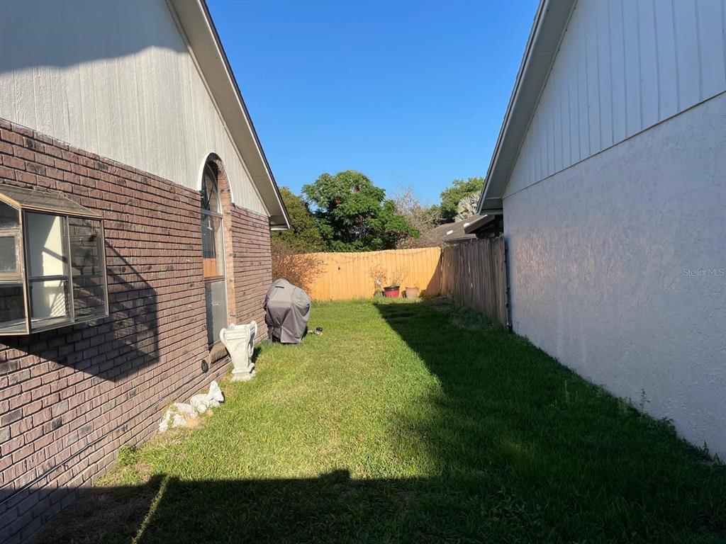 A narrow grassy side yard sits between a brick house and a white stucco house — 2158 PAPRIKA DRIVE, ORLANDO, FL