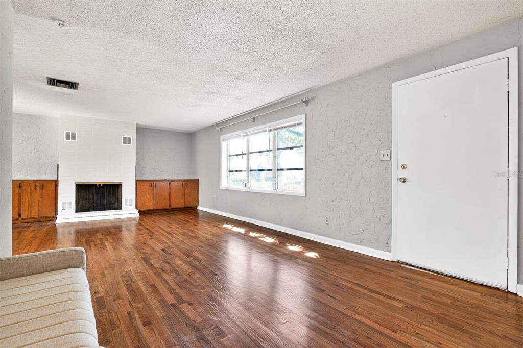 A living room with hardwood floors, a fireplace, built-in cabinets, and a white front door — 914 NE 11TH AVENUE, GAINESVILLE, FL