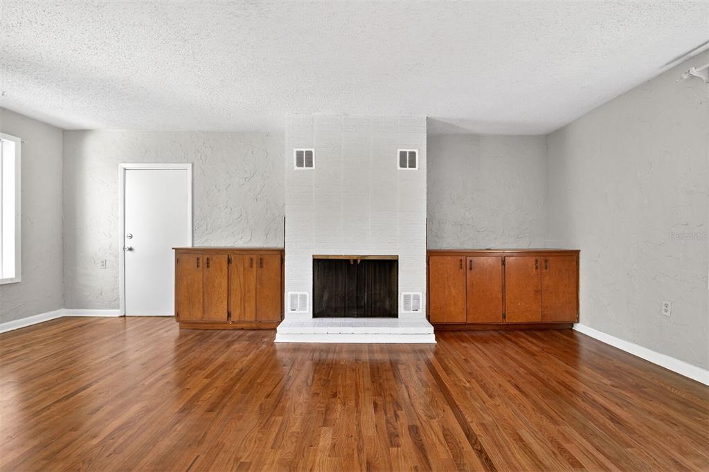 A living room features hardwood floors, a white brick fireplace, and built-in wooden cabinets — 914 NE 11TH AVENUE, GAINESVILLE, FL