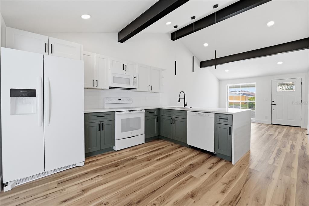 A kitchen with white upper cabinets, dark lower cabinets, white appliances, and exposed black beams — 8602 BRIAR GROVE CIR, TAMPA, FL