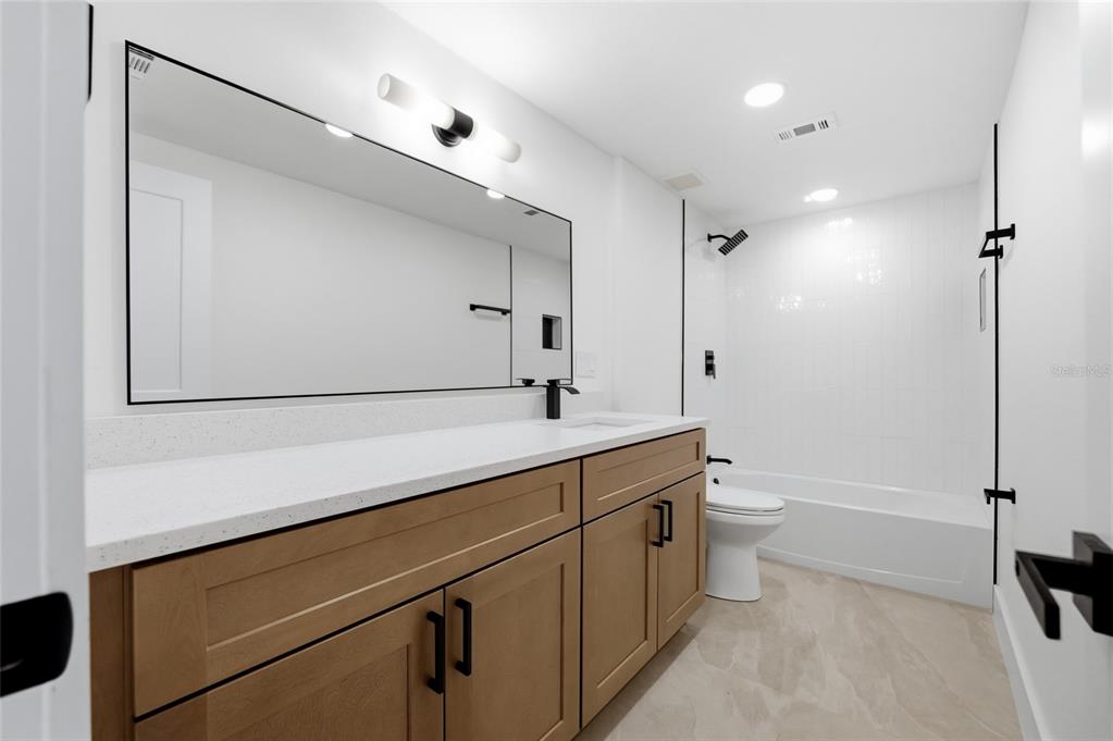 A modern bathroom features a light wood vanity, white countertop, large mirror, and shower-tub combo — 8602 BRIAR GROVE CIR, TAMPA, FL