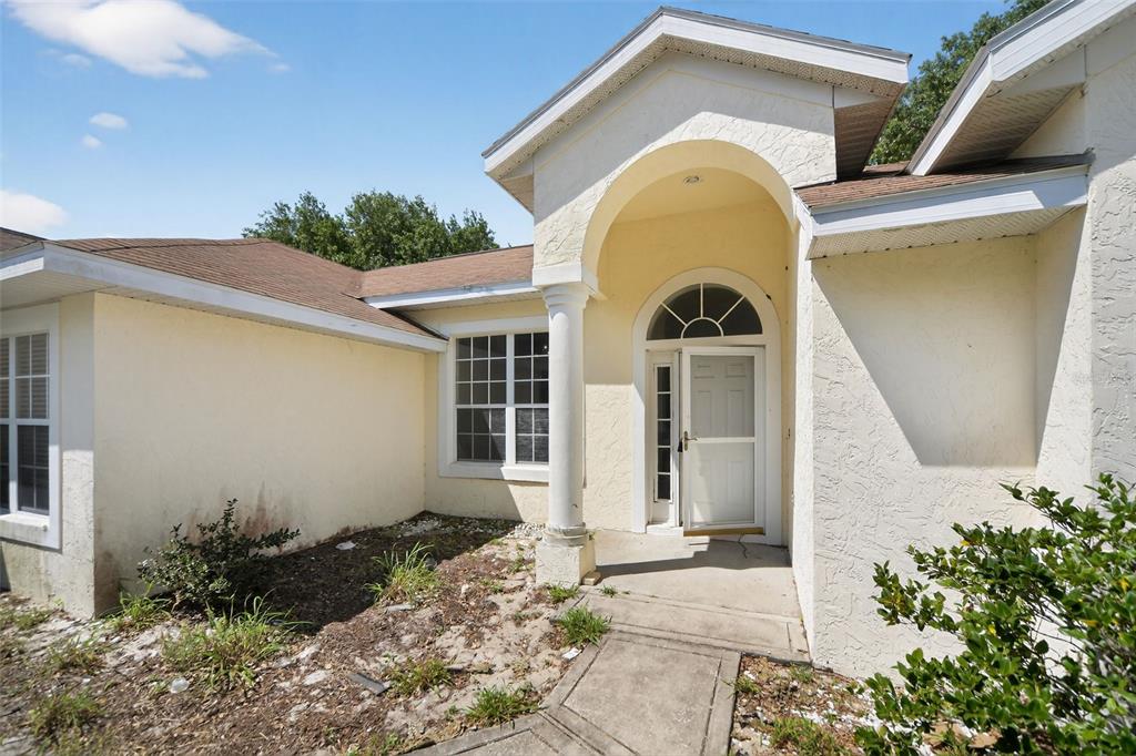 A tan stucco house exterior features a covered entryway with a column and arched window — 2518 MAYWOOD STREET, EUSTIS, FL