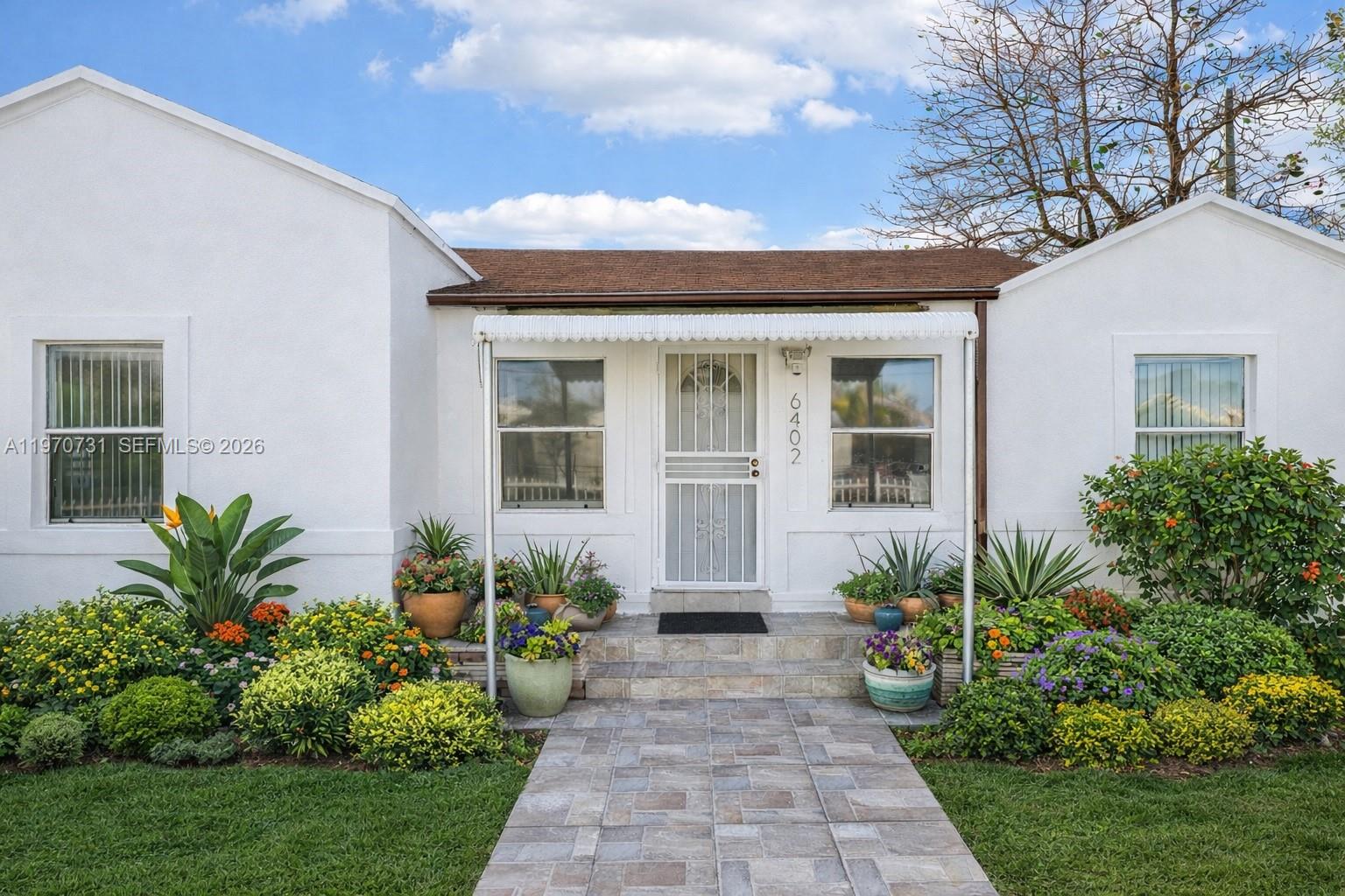 A white house with a tiled walkway, a metal awning, and a lush front garden — 6402 NW 8th Ave, Miami FL 33150, MIAMI, FL