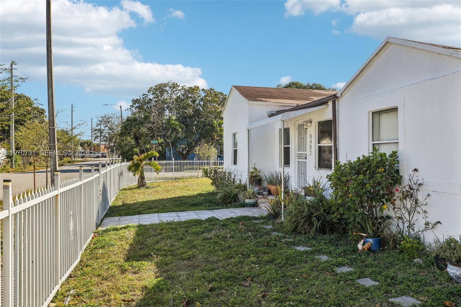 A white single-story house features a fenced yard, a tiled walkway, and various potted plants — 6402 NW 8th Ave, Miami FL 33150, MIAMI, FL