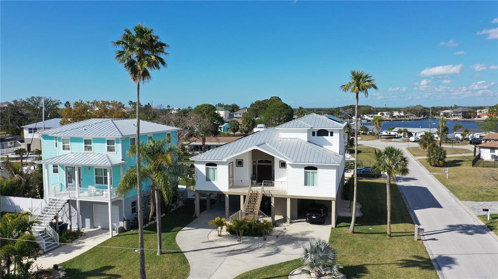 An aerial view shows two elevated houses with metal roofs and palm trees nearby — 8117 BRIGHTON DRIVE, PORT RICHEY, FL