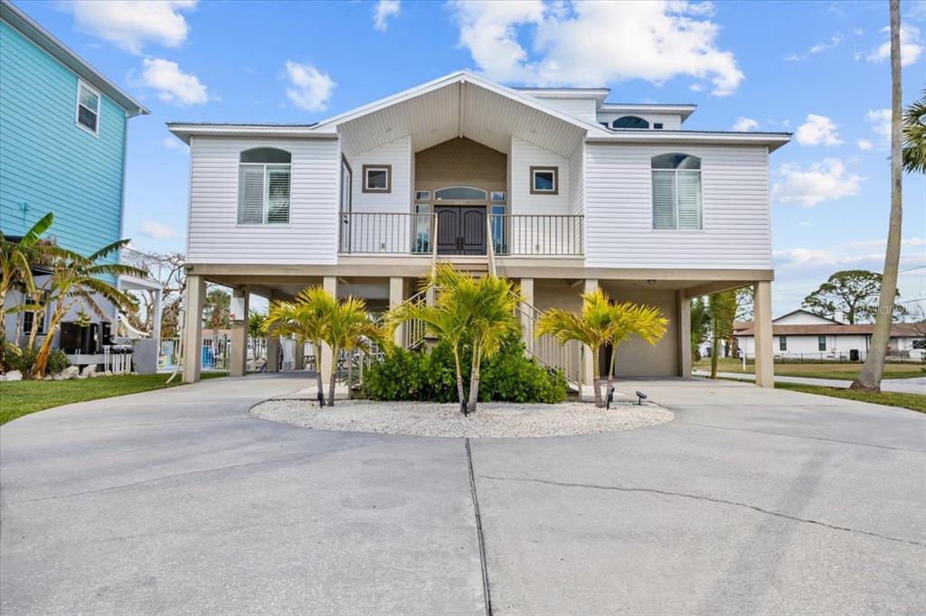 A white elevated house with a front balcony, concrete driveway, and palm trees — 8117 BRIGHTON DRIVE, PORT RICHEY, FL