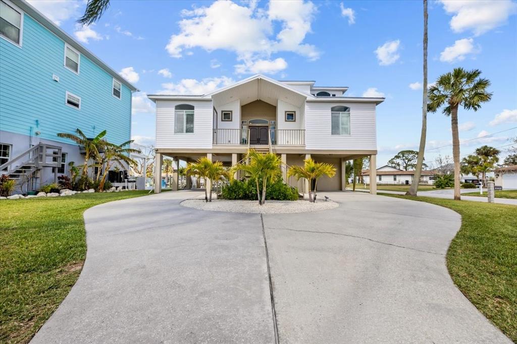 A white elevated house with a circular driveway and palm trees under a blue sky — 8117 BRIGHTON DRIVE, PORT RICHEY, FL
