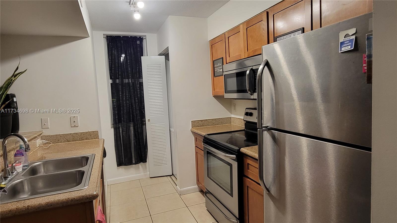 A galley kitchen features stainless steel appliances, wood cabinets, and tan countertops — 219 NW 12th Ave # 1004, Miami FL 33128, MIAMI, FL