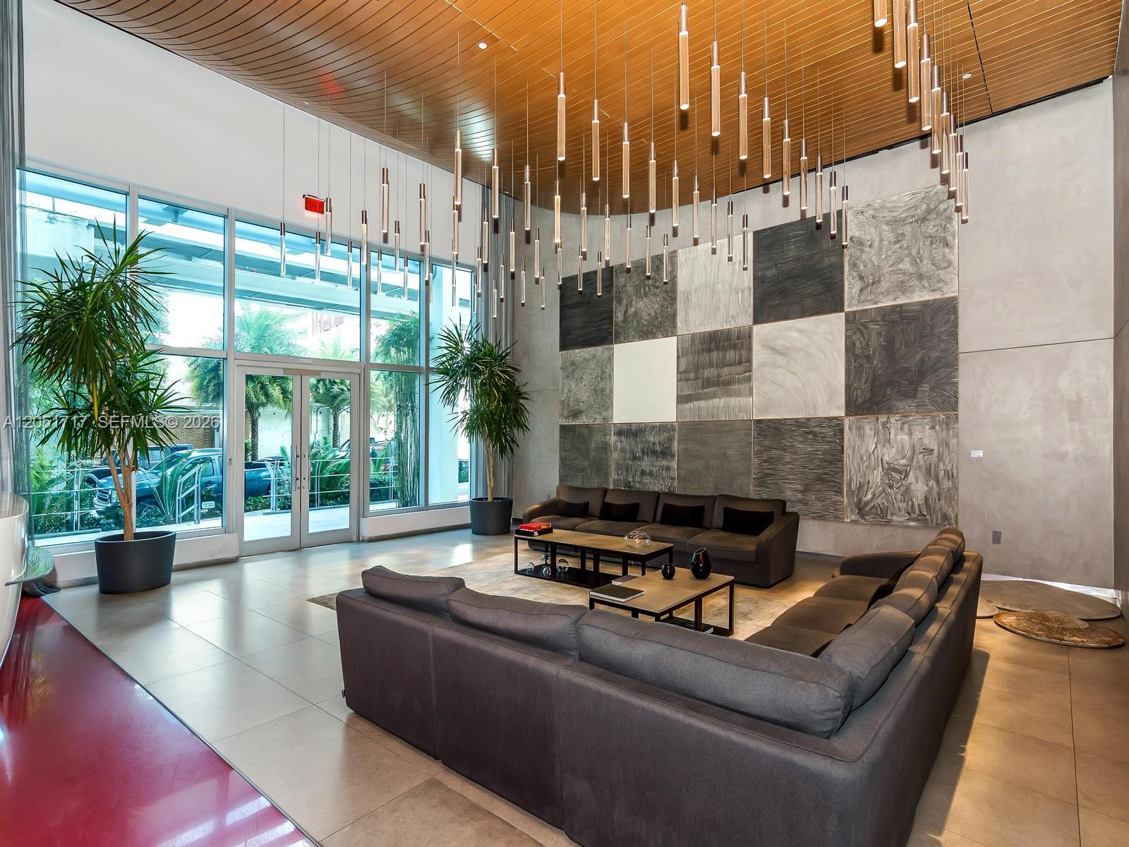 A modern lobby features a large grid art installation, dark sofas, and hanging pendant lights — 1100 S Miami Ave # 1504, Miami FL 33130, MIAMI, FL