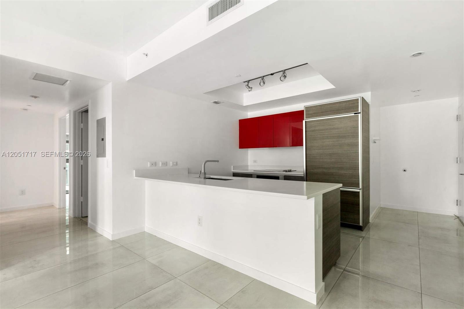 A modern kitchen features a white island, red cabinets, and a wood-paneled refrigerator — 1100 S Miami Ave # 1504, Miami FL 33130, MIAMI, FL