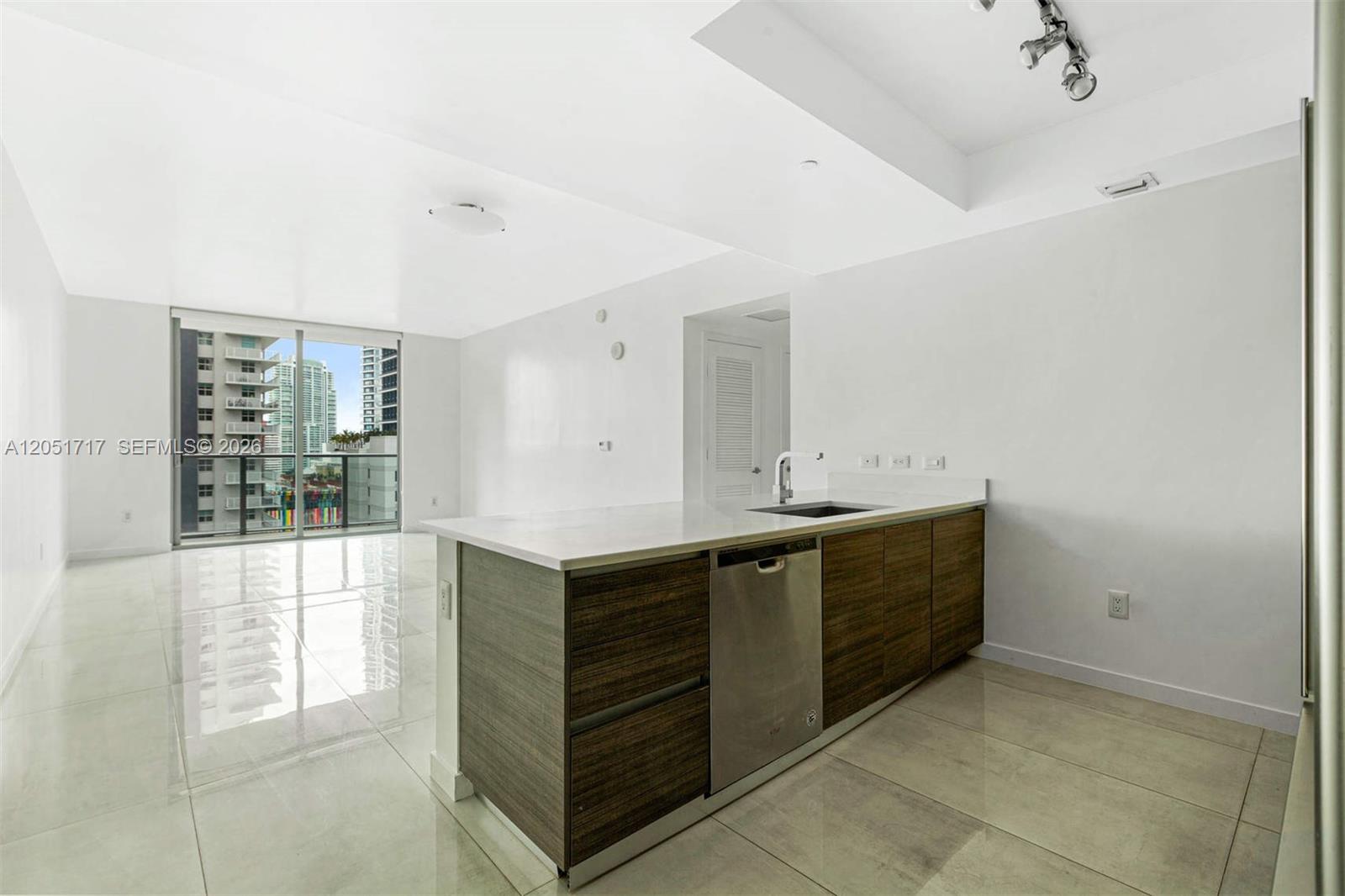 A modern kitchen island with wood cabinetry and a stainless steel dishwasher faces a balcony — 1100 S Miami Ave # 1504, Miami FL 33130, MIAMI, FL