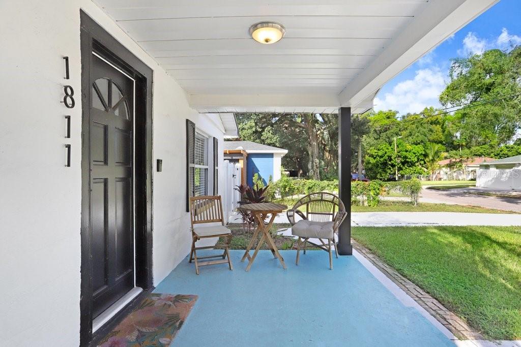 A covered front porch features a black door, blue flooring, and a small bistro set — 1811 E PALIFOX STREET, TAMPA, FL
