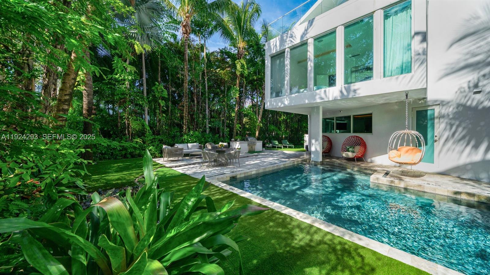 A modern white house features a backyard pool, patio seating, and a hanging chair — 480 Ocean Blvd, Golden Beach FL 33160, GOLDEN BEACH, FL