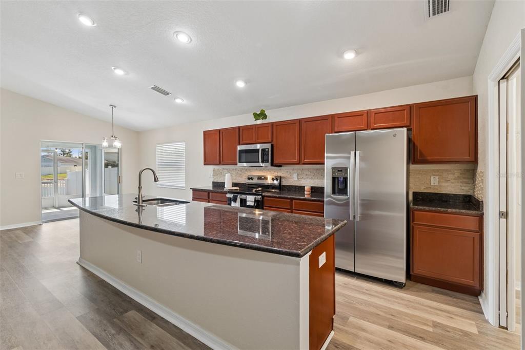 A kitchen features a granite-topped island, stainless steel appliances, and wood-toned cabinetry — 3042 GRAND PRESERVE BOULEVARD, MULBERRY, FL