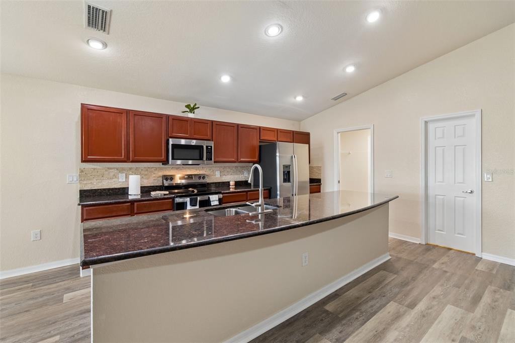 A kitchen features dark wood cabinets, granite countertops, a center island, and stainless steel appliances — 3042 GRAND PRESERVE BOULEVARD, MULBERRY, FL