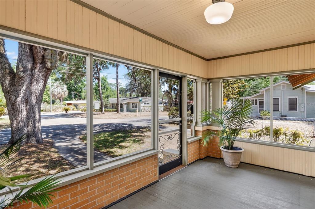A screened-in porch features brick walls, a gray floor, and large windows overlooking a street — 616 NE 7TH STREET, GAINESVILLE, FL