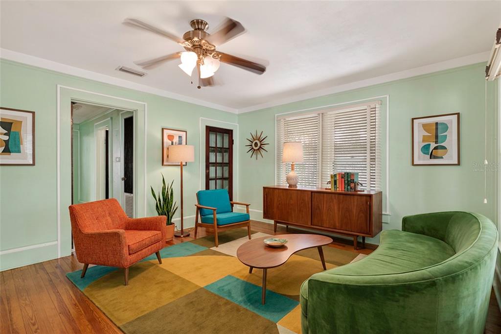 A mid-century modern living room features a green curved sofa, orange chair, and area rug — 616 NE 7TH STREET, GAINESVILLE, FL