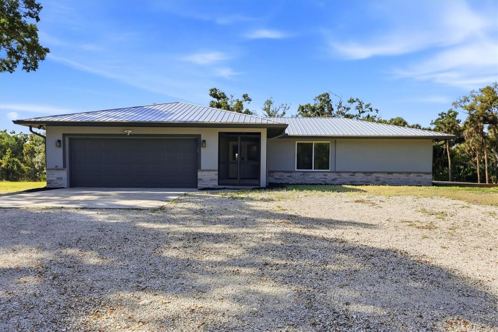 A single-story house with a metal roof, gray siding, stone accents, and a gravel driveway — 5361 MYAKKA VALLEY TRAIL, SARASOTA, FL