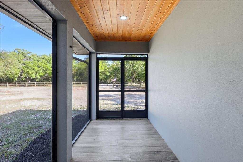 A screened-in porch features a wood-plank ceiling, light tile flooring, and a view of trees — 5361 MYAKKA VALLEY TRAIL, SARASOTA, FL