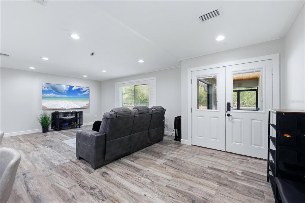 A living room features gray wood-look flooring, a gray reclining sofa, and double glass doors — 5361 MYAKKA VALLEY TRAIL, SARASOTA, FL