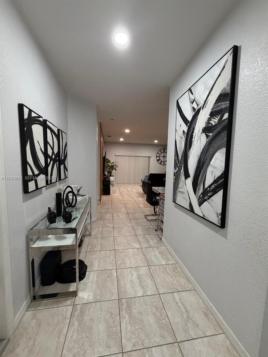 A hallway with tile flooring features abstract wall art and a glass console table — 25787 SW 127th Pl # 25787, Homestead FL 33032, HOMESTEAD, FL