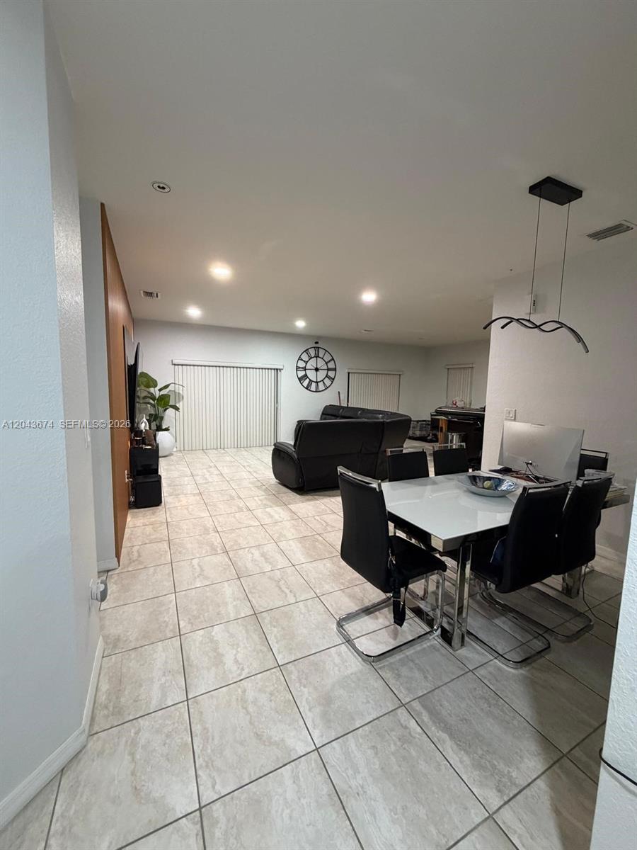 A dining area with a white table and black chairs sits before a living room — 25787 SW 127th Pl # 25787, Homestead FL 33032, HOMESTEAD, FL