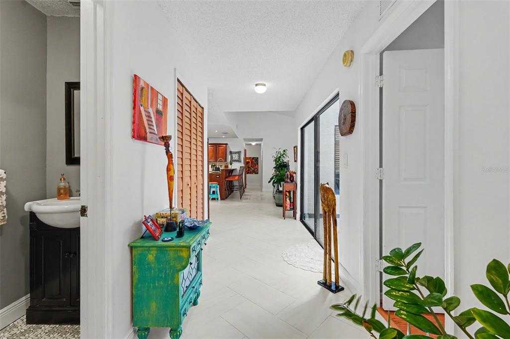 A bright hallway with white tile floors leads toward a kitchen with wooden cabinets — 2773 JEFFREY DRIVE, PALM HARBOR, FL