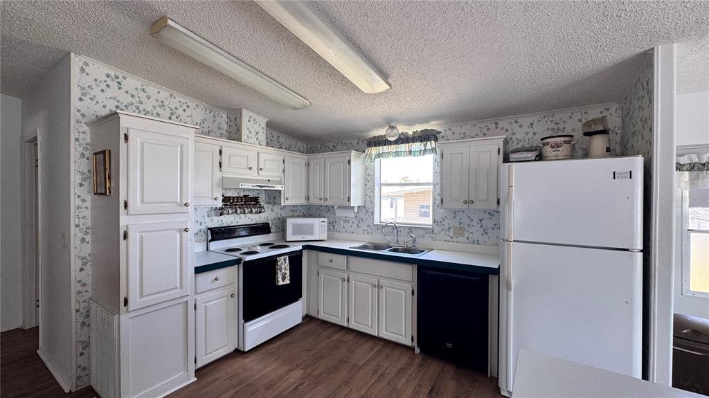 A kitchen features white cabinets, floral wallpaper, a black stove and dishwasher, and wood flooring — 236 RAMSGATE WAY, HAINES CITY, FL