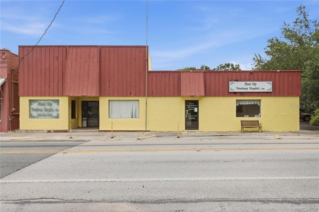 A yellow commercial building with a red metal roof sits along a paved road — 8307 E ORANGE AVENUE, FLORAL CITY, FL