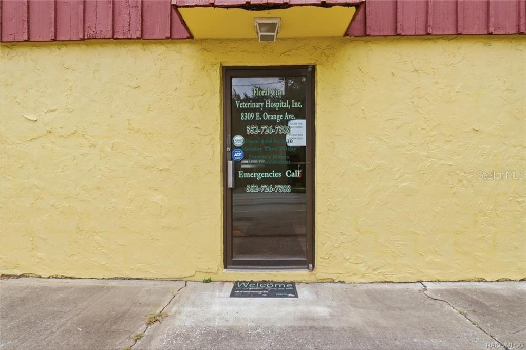 The exterior of a building features a yellow stucco wall and a glass entry door — 8307 E ORANGE AVENUE, FLORAL CITY, FL
