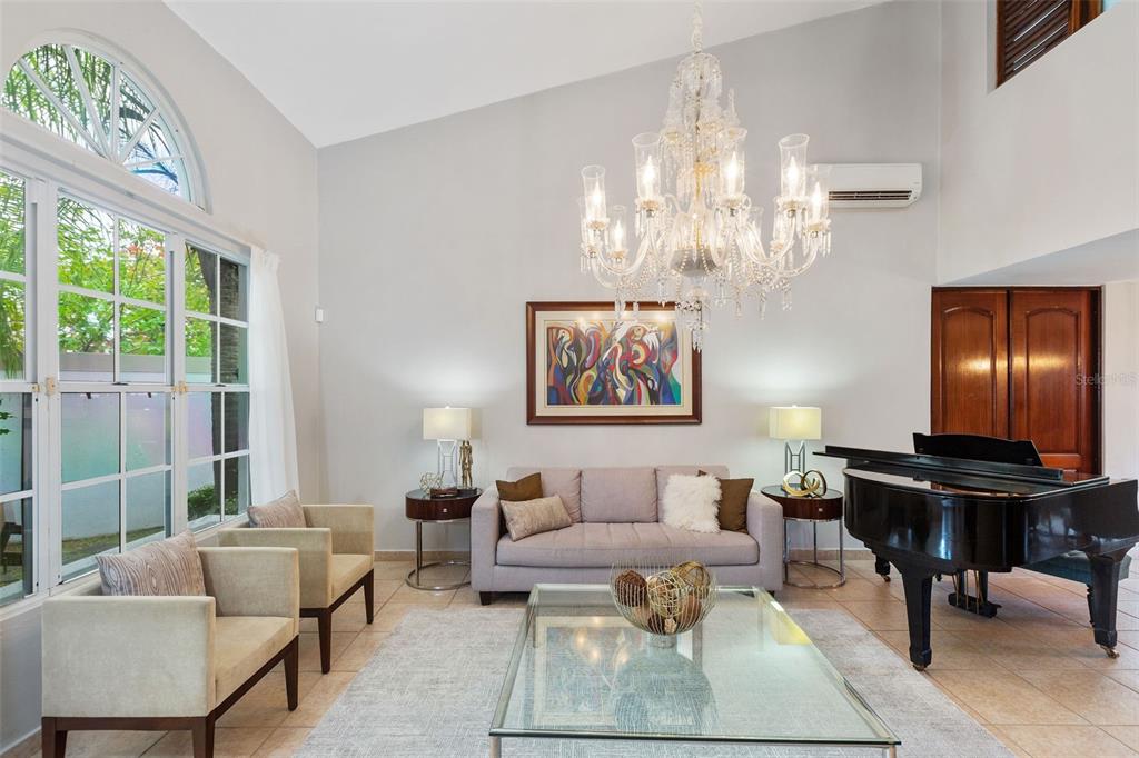 A living room features a grand piano, a crystal chandelier, and a large glass coffee table — Palma Real PALMA DE COCO, GUAYNABO, PR