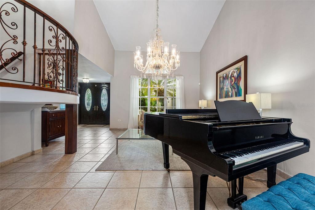 A grand piano sits in a tiled foyer featuring a curved staircase and crystal chandelier — Palma Real PALMA DE COCO, GUAYNABO, PR