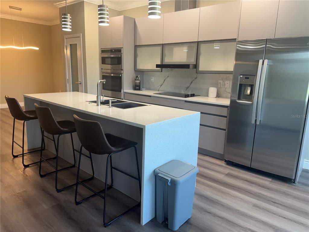 A modern kitchen features a white waterfall island, stainless steel appliances, and gray cabinetry — 2037 GREENBRIAR TERRACE, DAVENPORT, FL
