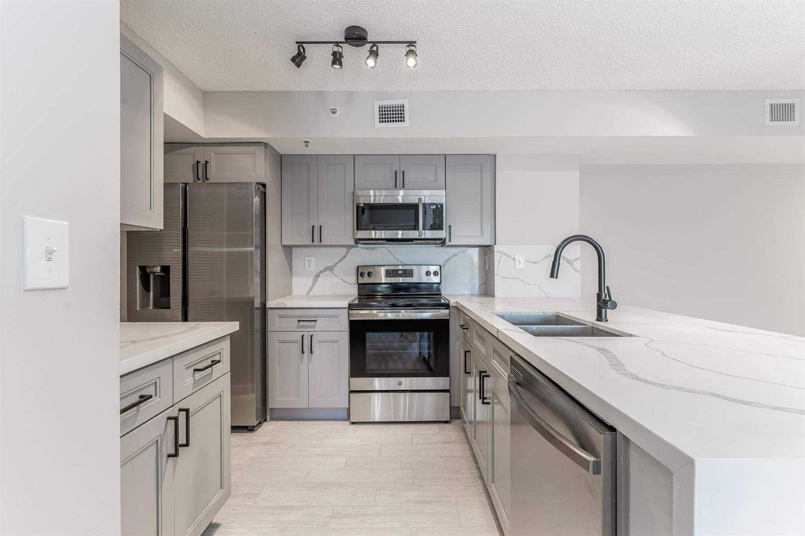 A modern kitchen features gray cabinets, stainless steel appliances, and white marble-patterned countertops — 2600 S University Drive # 208, Davie FL 33328, DAVIE, FL