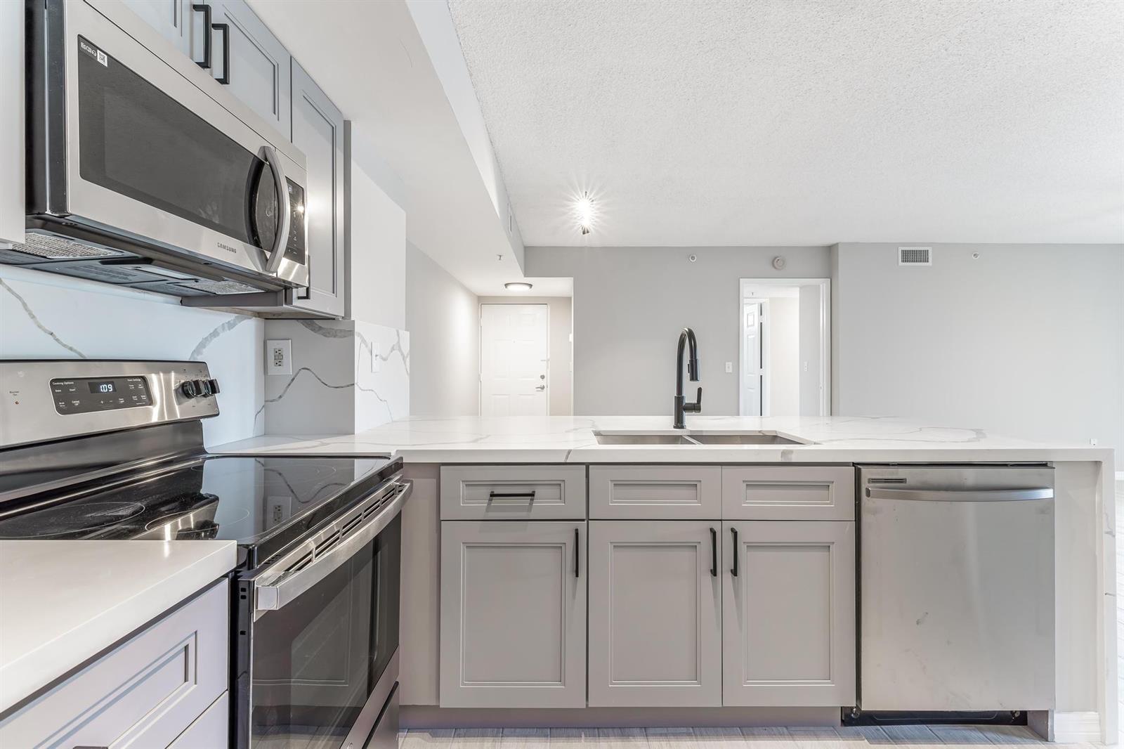 A kitchen features grey cabinets, stainless steel appliances, and white marble-look countertops — 2600 S University Drive # 208, Davie FL 33328, DAVIE, FL