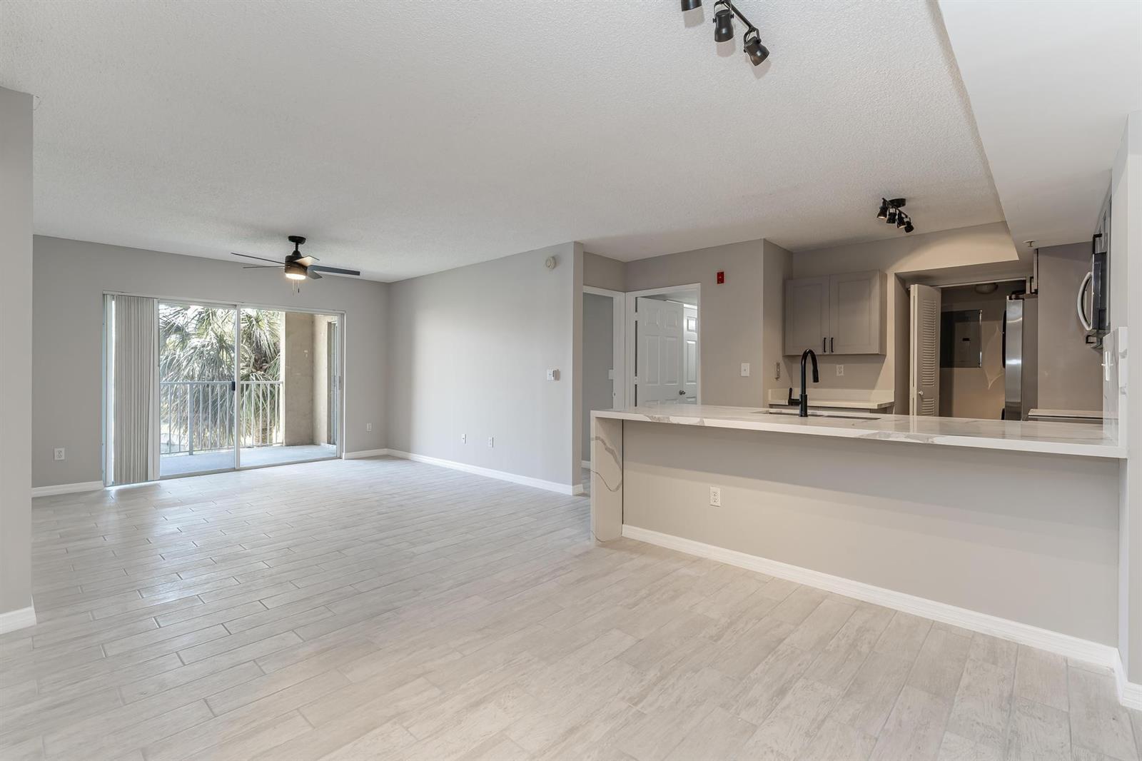 An open-concept living area features light-colored tile flooring, a kitchen island, and a sliding glass door — 2600 S University Drive # 208, Davie FL 33328, DAVIE, FL