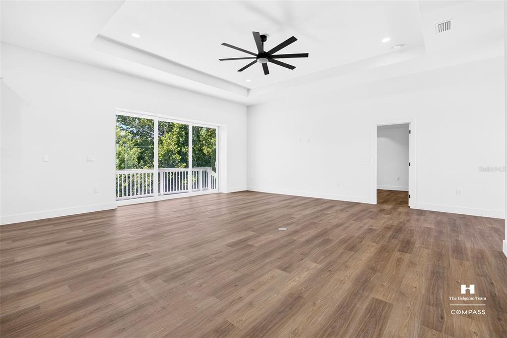 A spacious, minimalist living room features white walls, wood-look flooring, a tray ceiling, and sliding doors — 641 BONITA COURT, PUNTA GORDA, FL