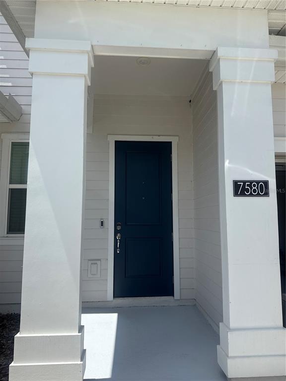 A dark blue front door is framed by two white columns on a concrete porch — 7580 STONE CREEK TRAIL, KISSIMMEE, FL