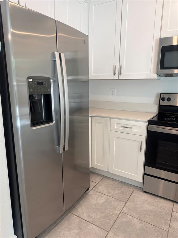 A kitchen features stainless steel appliances, white cabinets, and light-colored tile flooring — 7580 STONE CREEK TRAIL, KISSIMMEE, FL