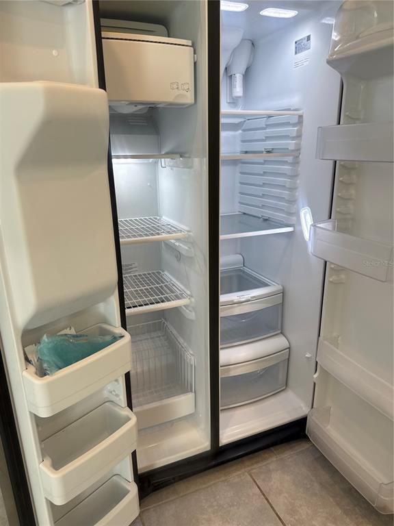 An open side-by-side refrigerator with white interior shelving and drawers — 7580 STONE CREEK TRAIL, KISSIMMEE, FL