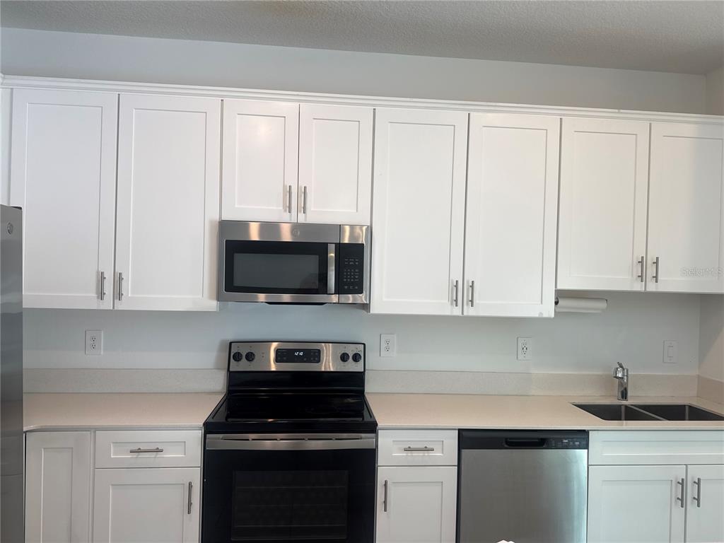 A kitchen features white cabinets, stainless steel appliances, and light-colored countertops — 7580 STONE CREEK TRAIL, KISSIMMEE, FL
