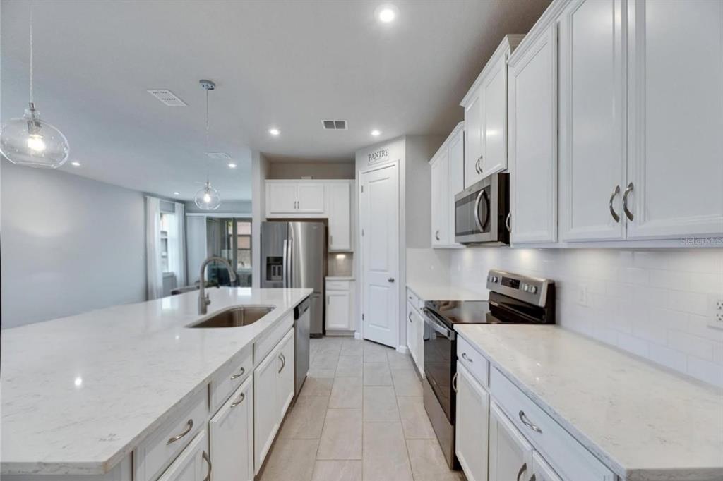 A modern kitchen features white cabinets, quartz countertops, stainless steel appliances, and a large island — 3719 LAUGHING DOVE AVENUE, SUN CITY CENTER, FL