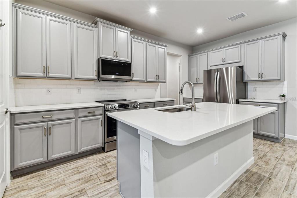 A kitchen with gray cabinets, white countertops, stainless steel appliances, and a central island — 3719 LAUGHING DOVE AVENUE, SUN CITY CENTER, FL