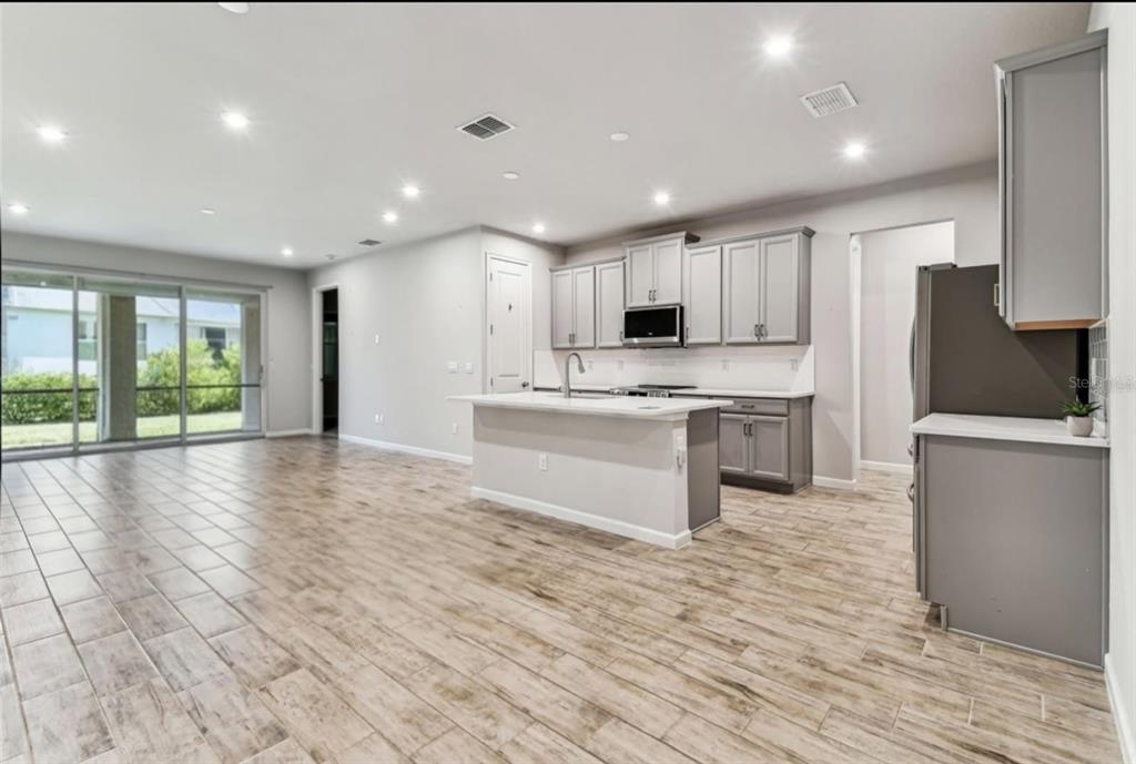 A kitchen with gray cabinets and a central island opens into a living area — 3719 LAUGHING DOVE AVENUE, SUN CITY CENTER, FL