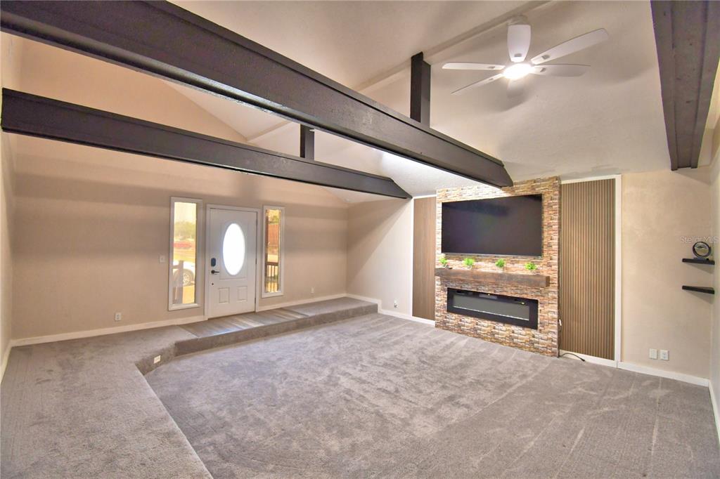 A sunken living room features a stone fireplace, a wall-mounted television, and exposed ceiling beams — 208 CENTER STREET, AUBURNDALE, FL