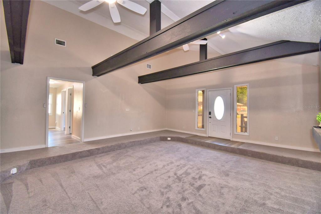 A sunken living room features dark exposed ceiling beams, gray carpeting, and a white front door — 208 CENTER STREET, AUBURNDALE, FL