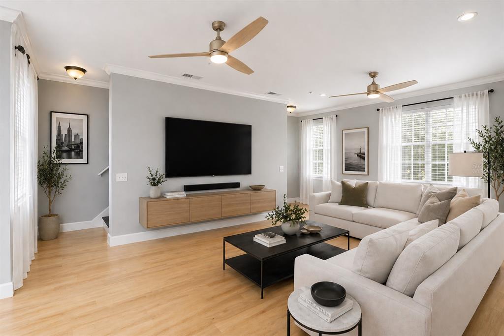 A living room features light wood floors, a wall-mounted TV, a sectional sofa, and ceiling fans — 2611 ESPANA COURT, TAMPA, FL